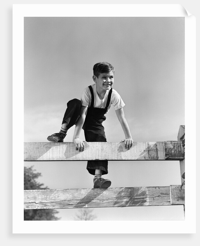1940s brunette boy wearing overalls climbing over fence by Anonymous