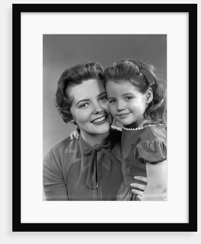1950s girl daughter smiling hugging woman mother cheek to cheek together by Anonymous