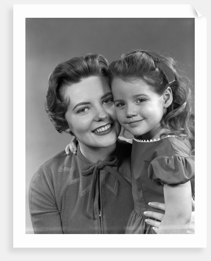 1950s girl daughter smiling hugging woman mother cheek to cheek together by Anonymous