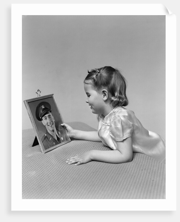1940s child little girl looking at framed picture of her father a soldier in uniform by Anonymous