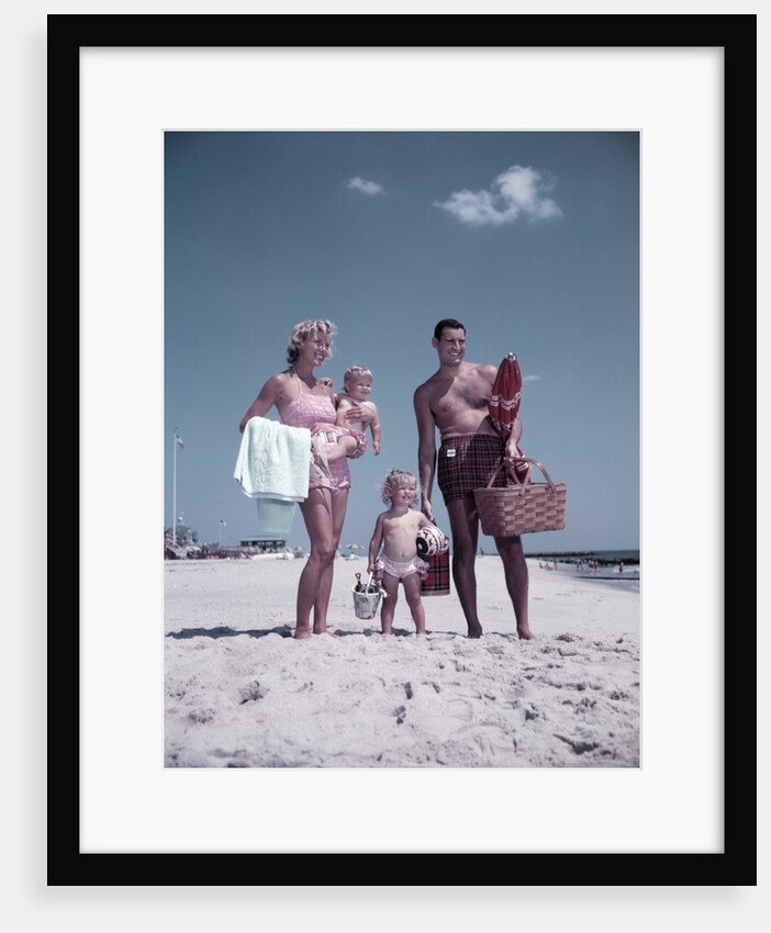 1950s family man woman mother father children boy girl son daughter standing sandy beach with toys and picnic basket by Anonymous