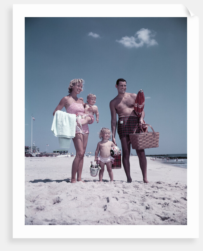 1950s family man woman mother father children boy girl son daughter standing sandy beach with toys and picnic basket by Anonymous