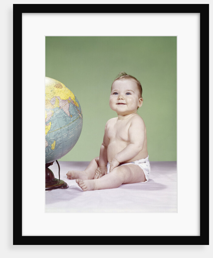 1960s smiling baby wearing diaper sitting beside earth globe by Anonymous