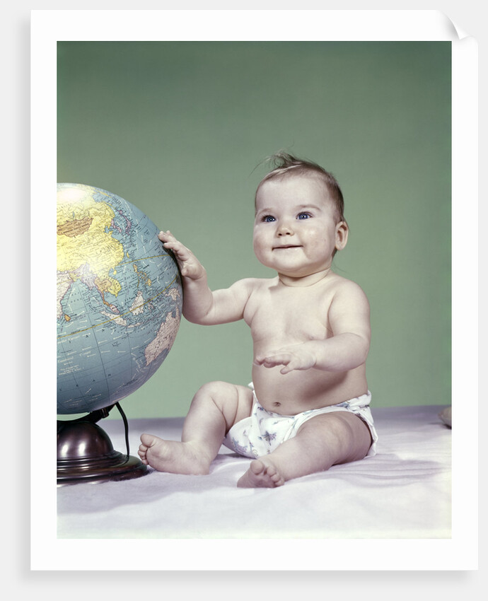 1960s smiling baby girl sitting in diapers hand touching world globe by Anonymous
