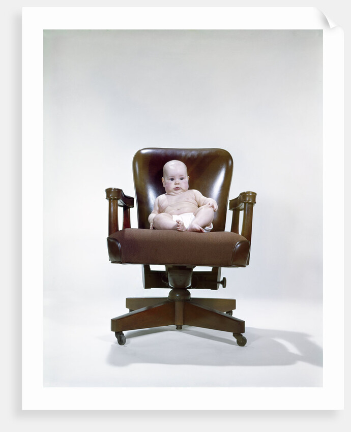1960s chubby baby in diaper sitting in office executive chair by Anonymous