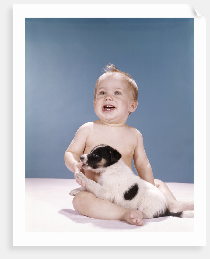 1960s smiling baby girl sitting in diapers playing with young black and white puppy dog by Anonymous