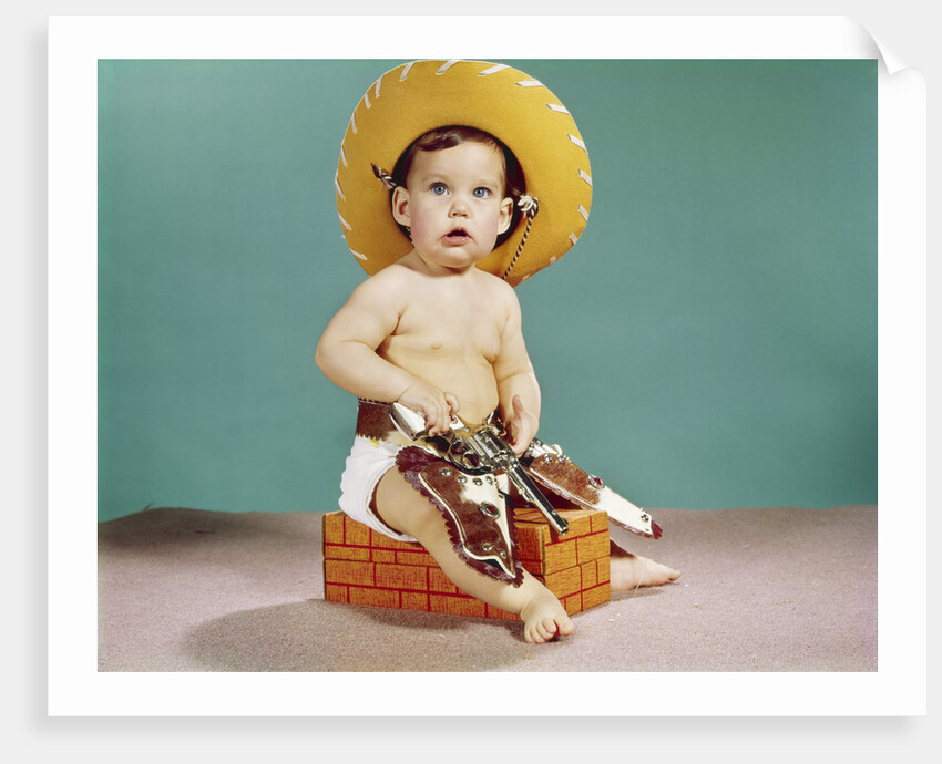 1960s baby wearing cowboy hat and holster with guns pistols looking at camera by Anonymous