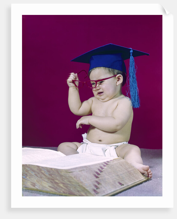1960s graduate baby wearing mortarboard eyeglasses reading book by Anonymous