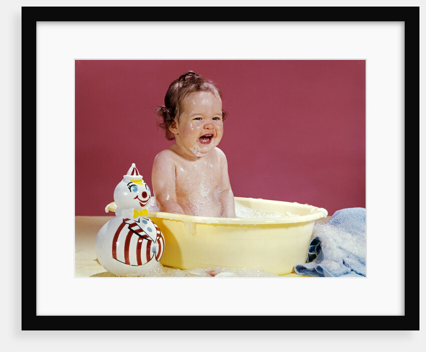 1960s crying brunette baby sitting in yellow plastic bath tub with toy clown by Anonymous