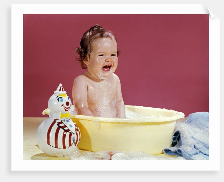 1960s crying brunette baby sitting in yellow plastic bath tub with toy clown by Anonymous