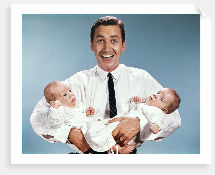 1960s smiling man father looking at camera holding twin babies infants by Anonymous