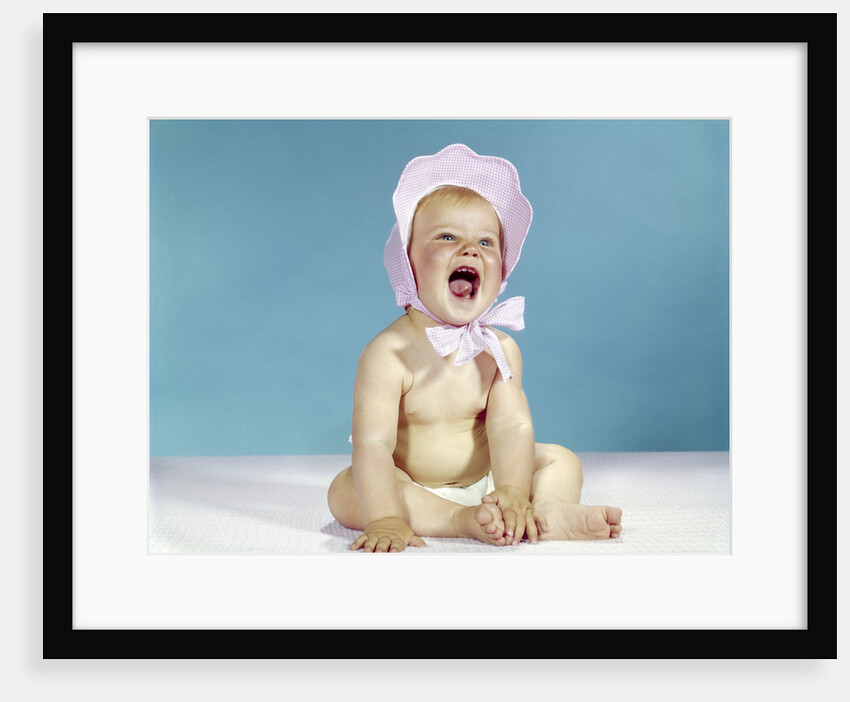 1960s baby wearing pink checked bonnet laughing by Anonymous
