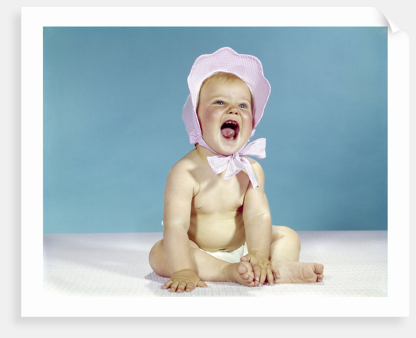 1960s baby wearing pink checked bonnet laughing by Anonymous
