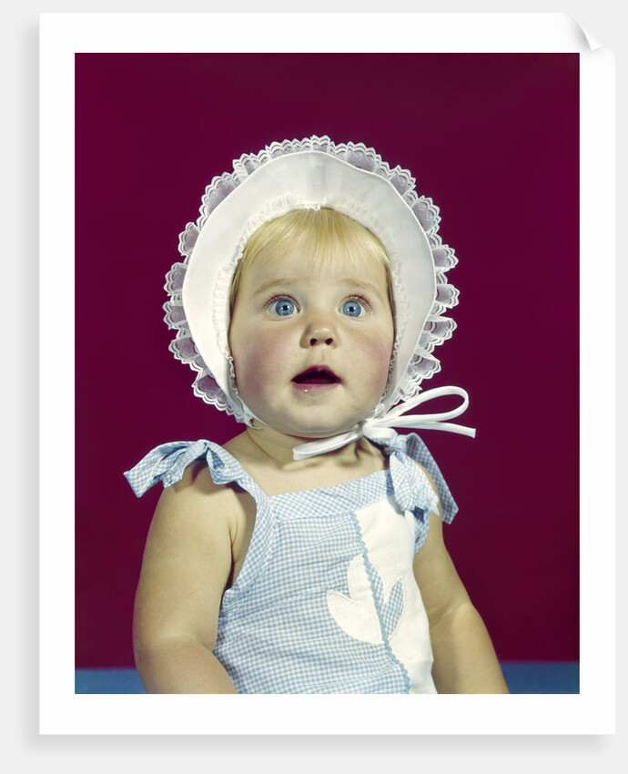 1960s blonde baby blue eyes wearing ruffled bonnet facial expression of wonder looking at camera by Anonymous