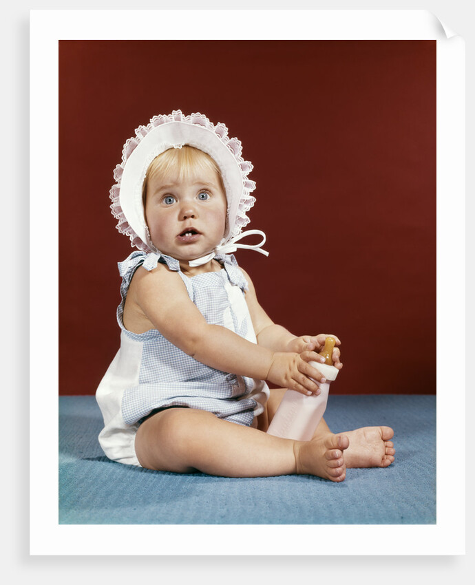 1960s baby girl ruffled bonnet holding bottle funny facial expression looking at camera by Anonymous
