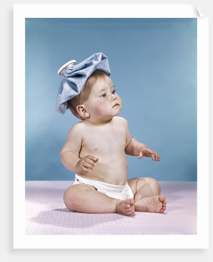 1960s baby sitting with ice pack on top of head by Anonymous