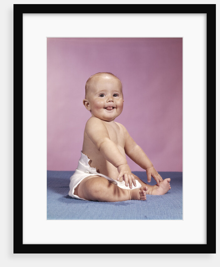 1960s smiling baby wearing cloth diaper sitting on blue blanket sticking out tongue looking at camera by Anonymous