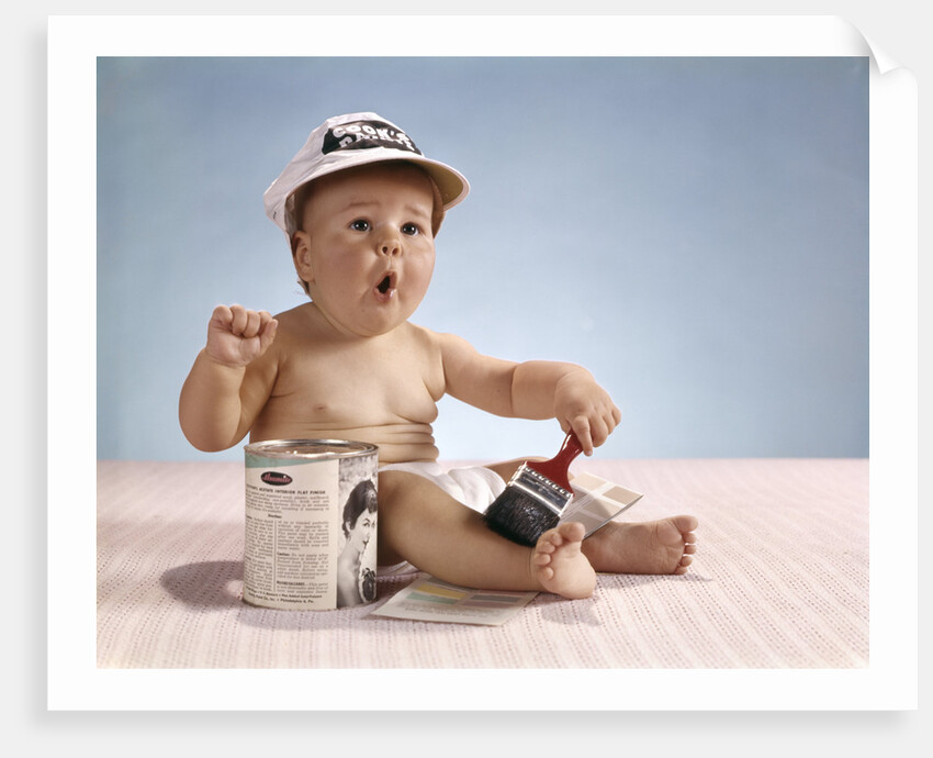1960s baby with funny facial expression wearing painters cap holding paintbrush sitting by paint can by Anonymous