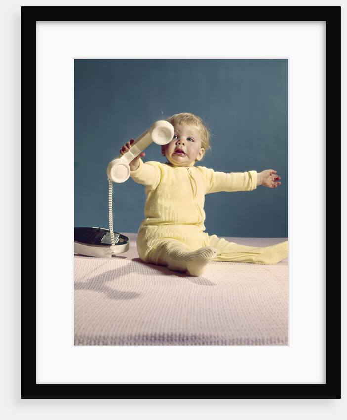 1960s baby holding telephone head set by Anonymous