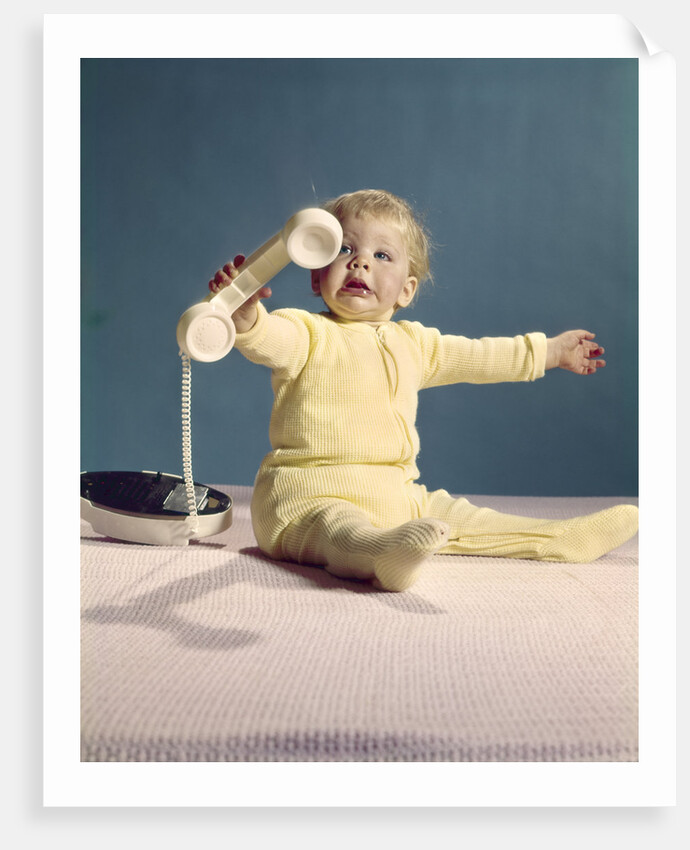 1960s baby holding telephone head set by Anonymous