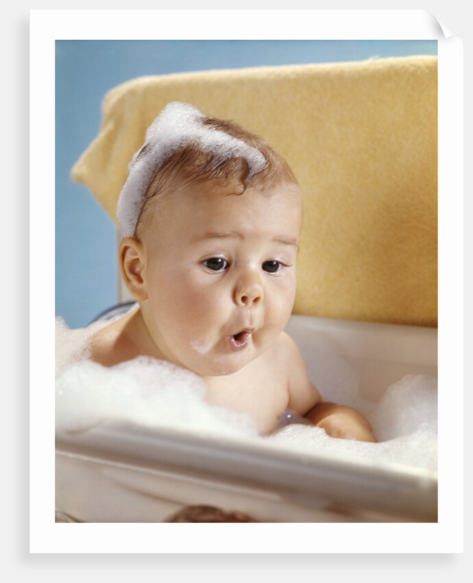 1960s baby with a surprised facial expression in bathtub covered with soap bubbles by Anonymous