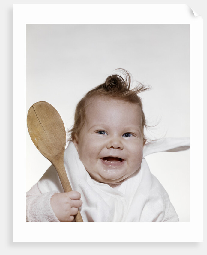 1960s 1970s smiling baby wearing bib and holding wooden spoon by Anonymous