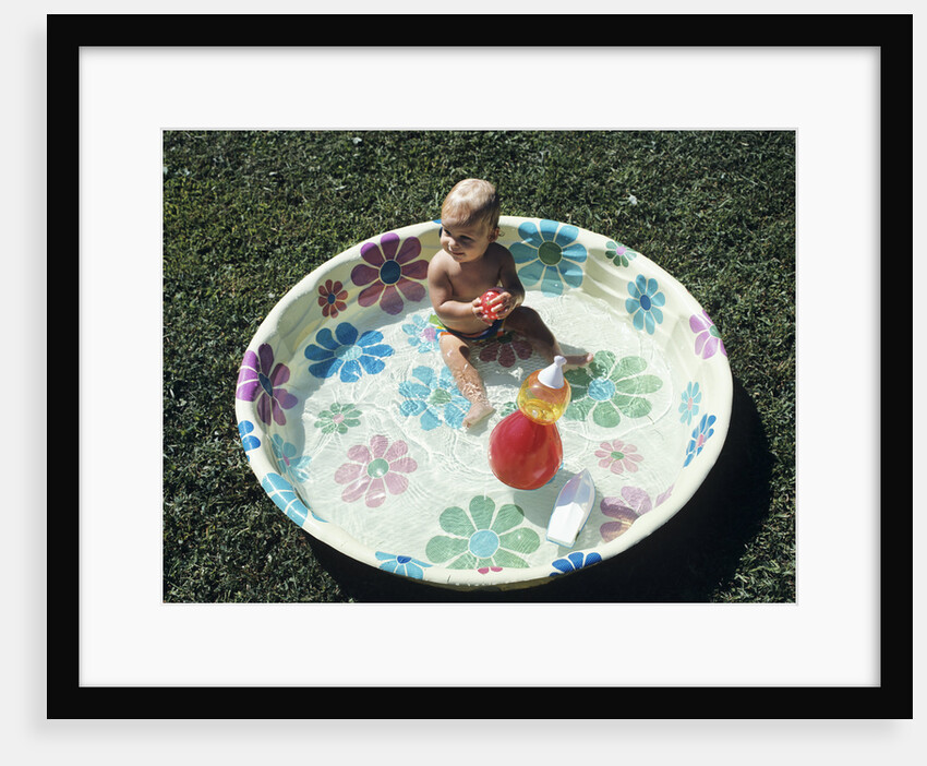 1970s baby sitting in plastic backyard kiddy pool viewed from above by Anonymous