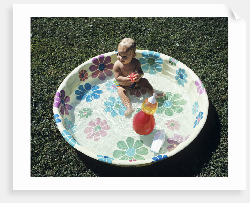 1970s baby sitting in plastic backyard kiddy pool viewed from above by Anonymous