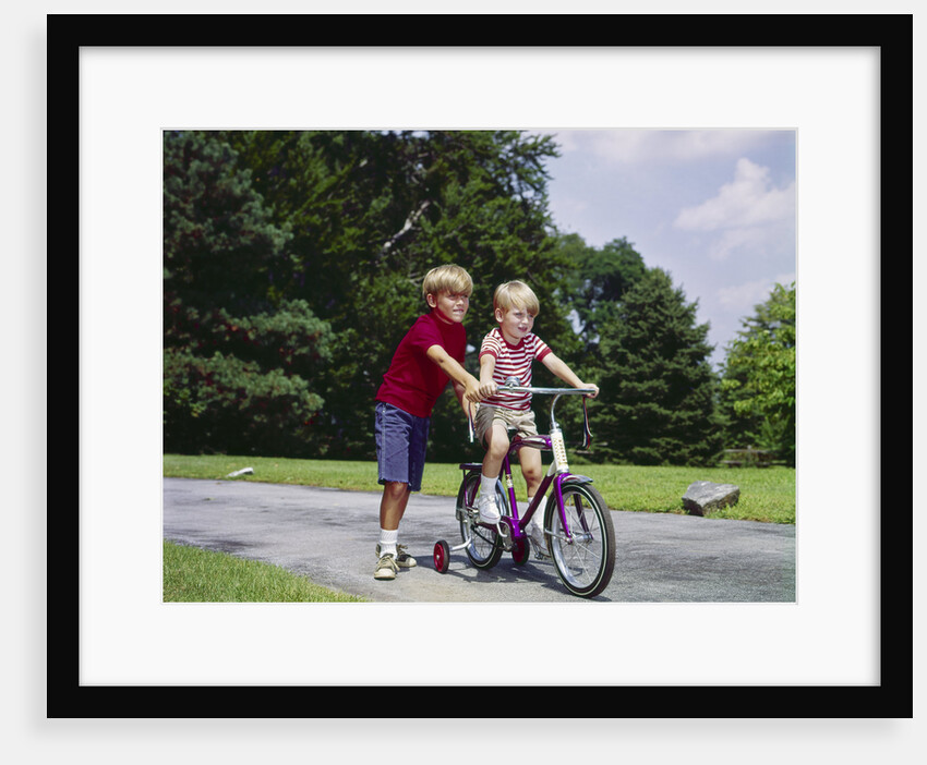 1960s 1970s boy helping little brother ride two wheel bicycle with training wheels by Anonymous
