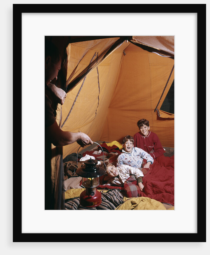 1960s father with lantern checking up on 3 boys in sleeping bags pajamas in tent by Anonymous