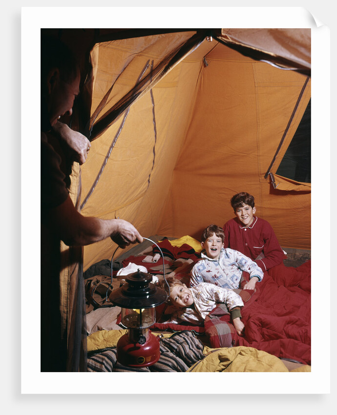 1960s father with lantern checking up on 3 boys in sleeping bags pajamas in tent by Anonymous