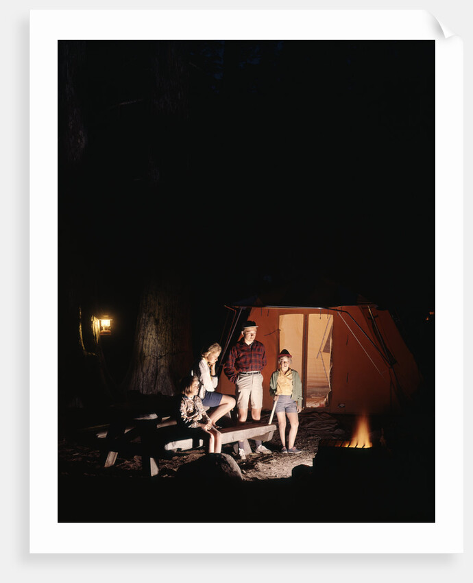 1960s night scene family gazing into campfire by tent by Anonymous