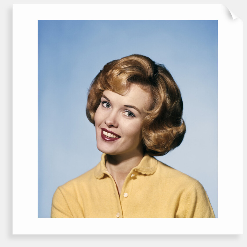 1960s smiling blond woman wearing a yellow sweater head tilted quizzical expression by Anonymous