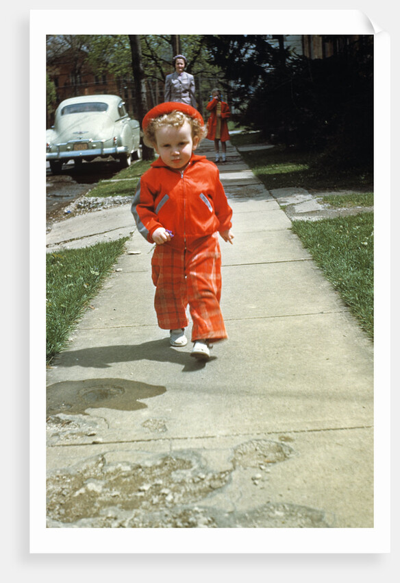 1950s little boy in red outfit running on pavement with mother just behind by Anonymous