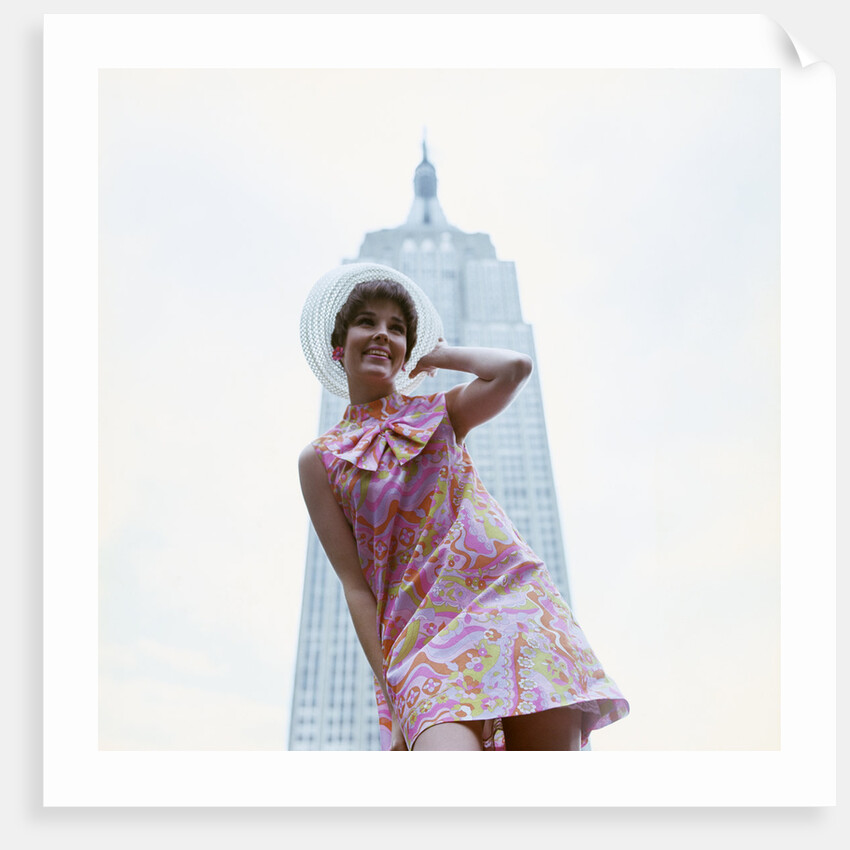 1960s young woman print miniskirt dress summer hat in front empire state building new york city by Anonymous