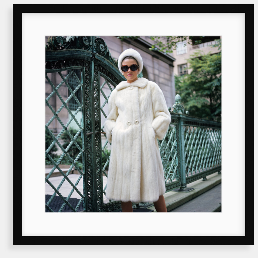 1960s woman wearing white mink fur coat hat sunglasses by wrought iron gate by Anonymous