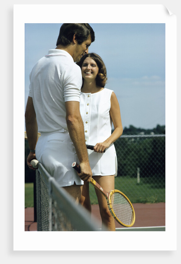 1970s smiling couple standing by net on tennis court holding wood rackets by Anonymous