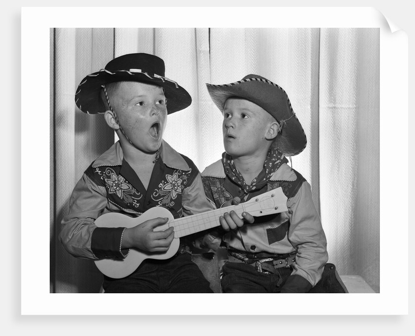 1950s 2 juvenile boys in cowboy hat & shirts playing ukulele & singing mouth open wide by Anonymous