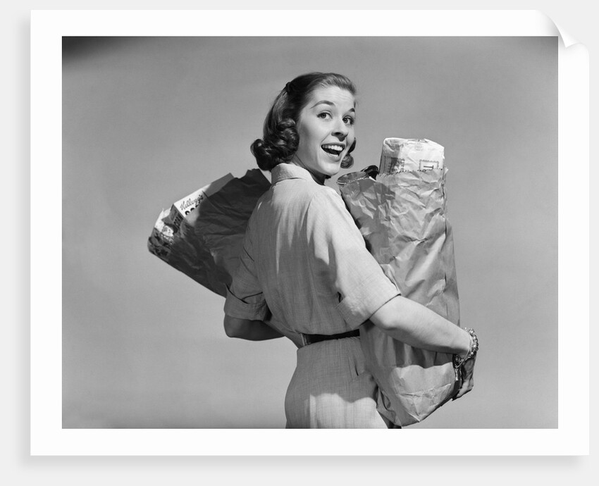 1950s smiling woman carrying grocery bags both hands looking at camera over her shoulder by Anonymous