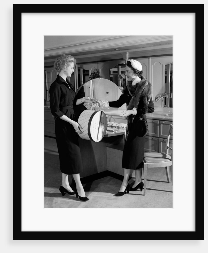 1950s woman in hat stole & gloves taking hatbox from saleswoman by Anonymous