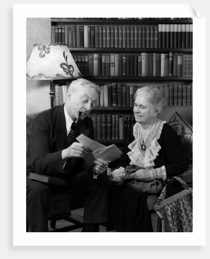 1930s 1940s retired senior couple looking at check in living room man smoking pipe by Anonymous