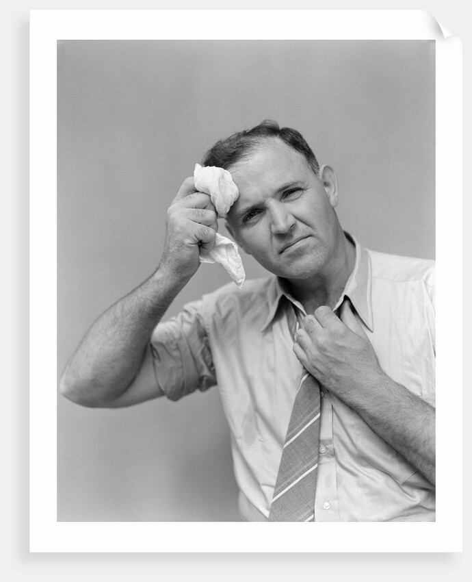 1940s 1950s perspiring man in rolled up shirt sleeves loosening tie holding handkerchief wiping forehead looking at camera by Anonymous
