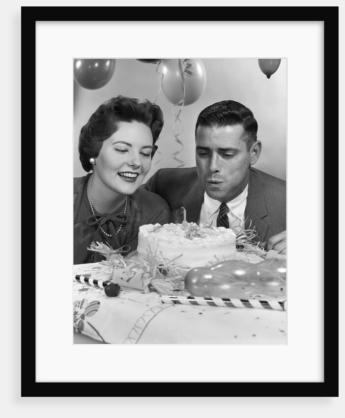 1950s 1960s couple with birthday anniversary cake man blowing out candle by Anonymous