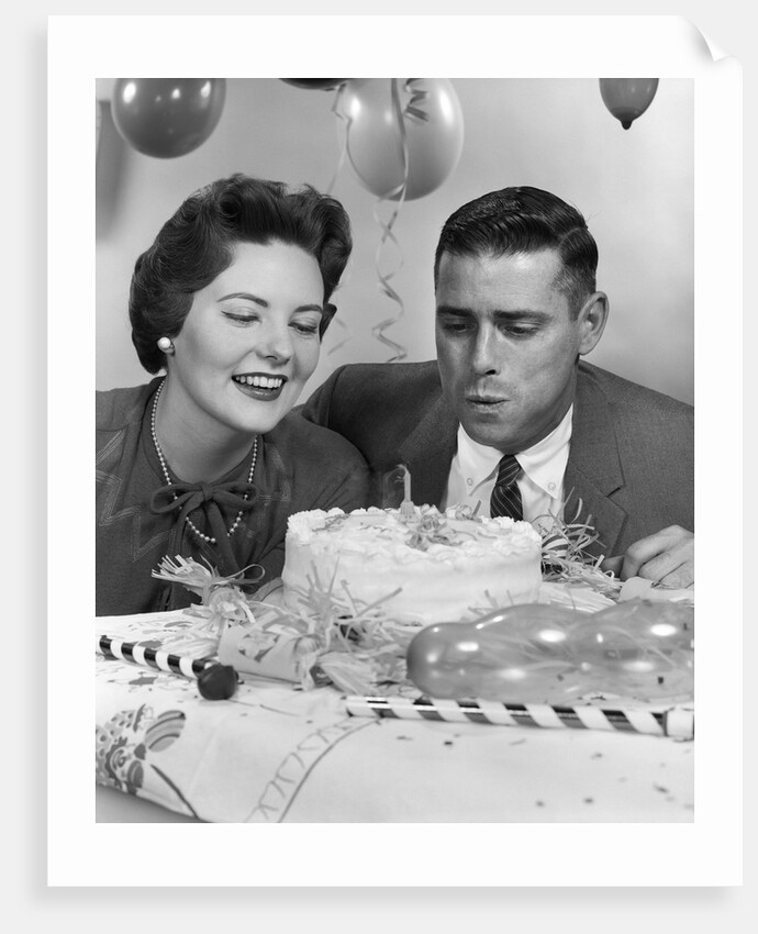 1950s 1960s couple with birthday anniversary cake man blowing out candle by Anonymous