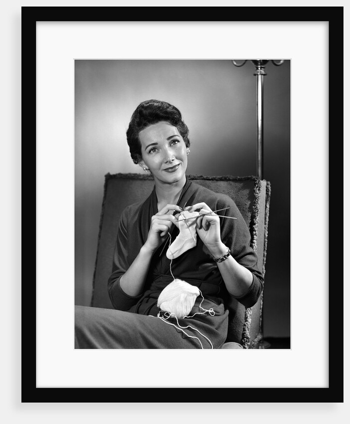 1950s woman crocheting baby sock looking at camera by Anonymous