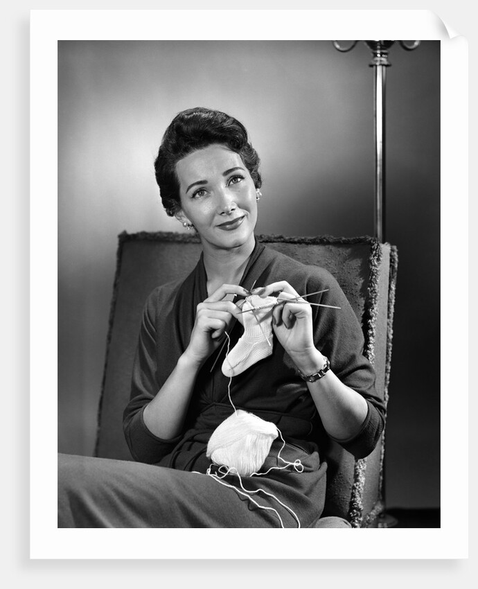 1950s woman crocheting baby sock looking at camera by Anonymous