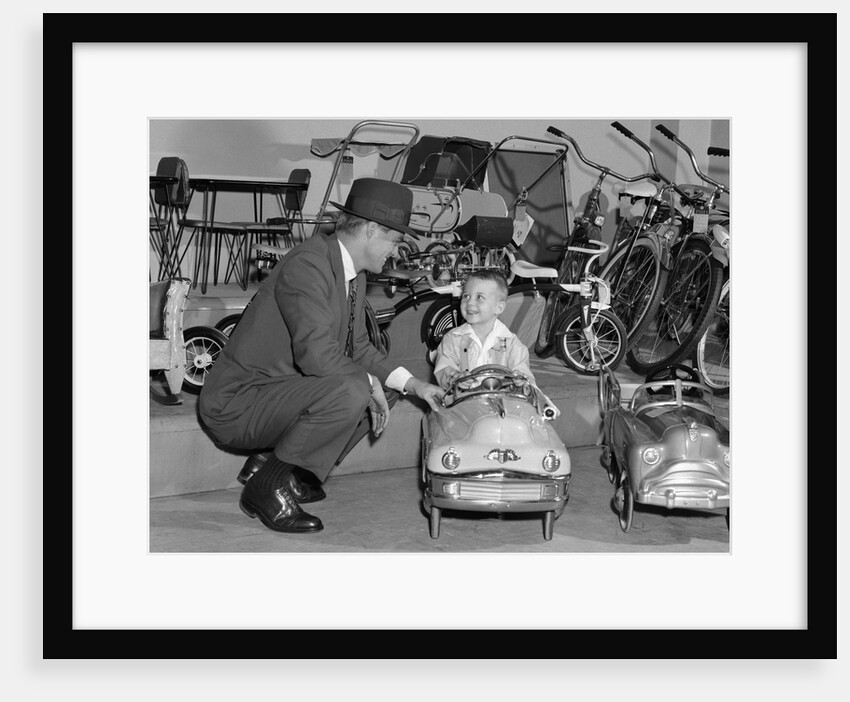 1950s father in toy store purchasing for son driving toy convertible peddle car by Anonymous