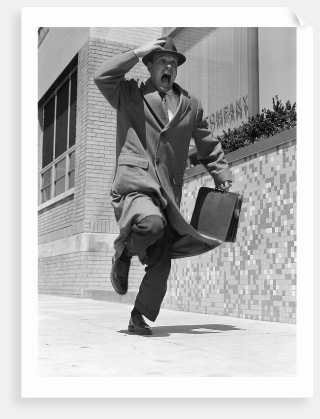 1960s 1950s frantic man running down street holding hat on with hand carrying briefcase wearing top coat by Anonymous