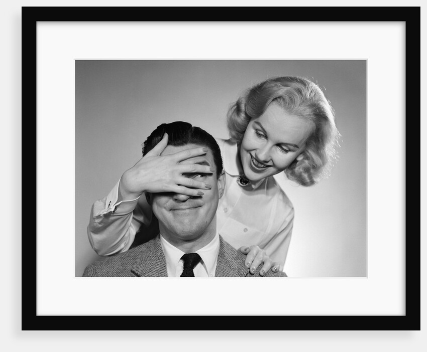 1950s woman standing behind man with hand over his eyes by Anonymous