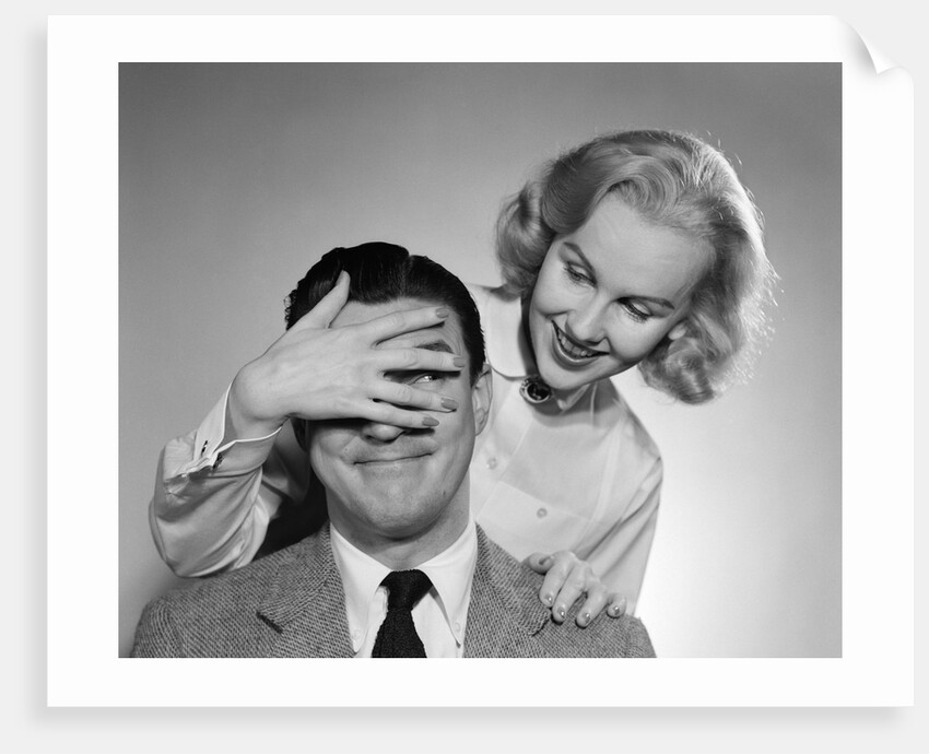 1950s woman standing behind man with hand over his eyes by Anonymous